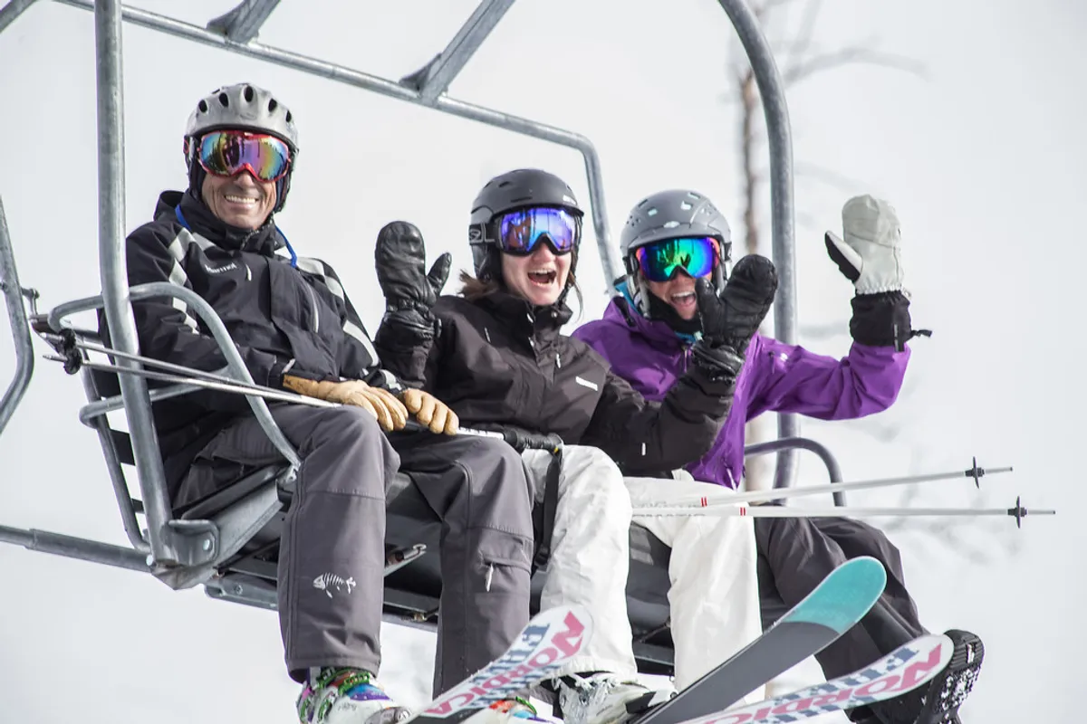 A lively winter scene with skiers riding a ski lift over a snowy landscape, surrounded by mountain scenery. The image encapsulates the exhilaration of world-class skiing and snowboarding, with a sense of camaraderie and adventure among participants.