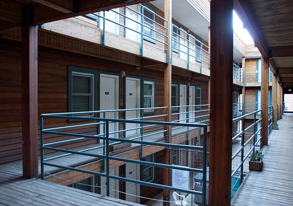 The image shows a communal interior area with wooden railings, doors leading to individual condos, and decorative planters. The space feels casual and encourages neighborly interaction, hinting at the communal and autonomous lifestyle emphasized in the section.