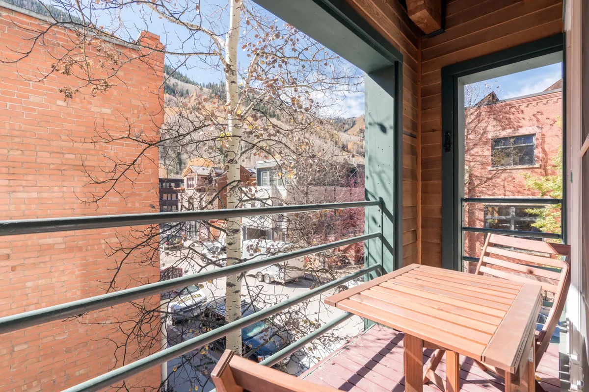 The photo captures a private balcony with a table and chairs looking out over a lively street and leafy trees. The view hints at the relaxing opportunities post-adventure: enjoying a drink, people-watching, or simply soaking in the changing scenery after a day outdoors.