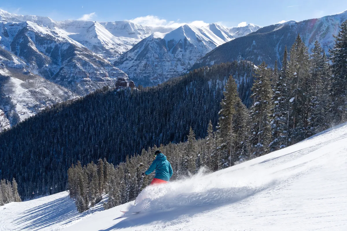 A snowboarder carves through fresh powder on snow-covered mountains, with evergreen trees in the background. The image radiates excitement and camaraderie—the kind of shared adventure that defines memorable group trips.