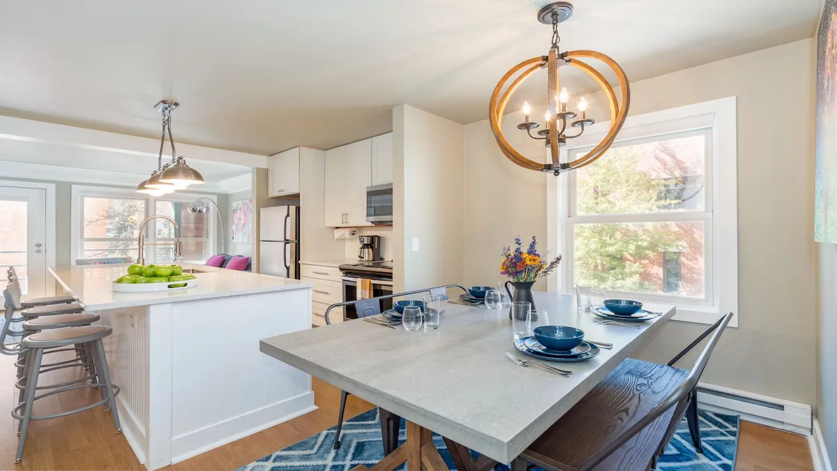 The image showcases a beautifully appointed dining area with a modern chandelier, a dining table elegantly set with plates and glasses, and a sleek kitchen island with comfortable bar stools. The warm lighting and stylish decor create an inviting space ideal for family gatherings and entertaining.