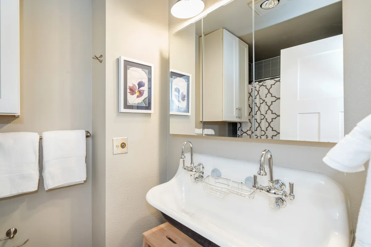 A stylish bathroom corner with a vintage-style sink, floral artwork, and modern lighting. The setup suggests a serene spot for self-care routines, with a blend of charm and practicality.